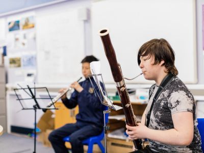 A boy plays the bassoon. He is wearing a white and grey tie-dye t-shirt